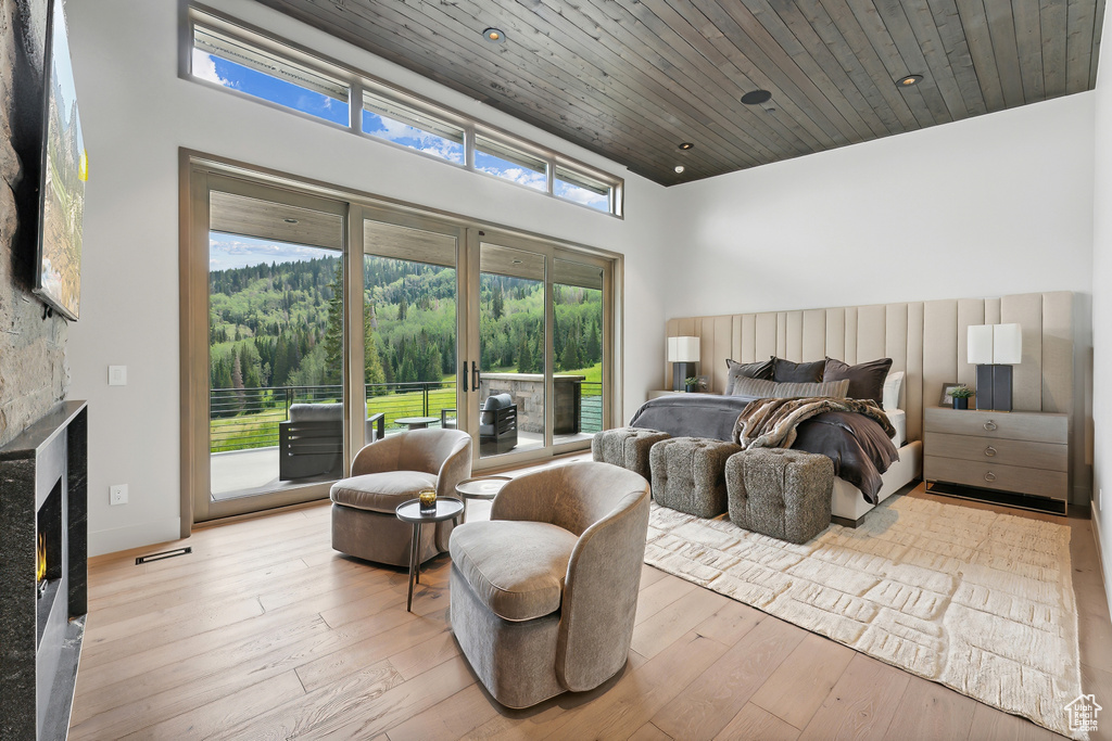 Bedroom with wood ceiling, access to exterior, light hardwood / wood-style flooring, and a stone fireplace