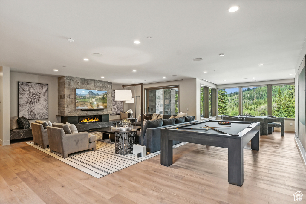 Recreation room with pool table, a stone fireplace, and light wood-type flooring