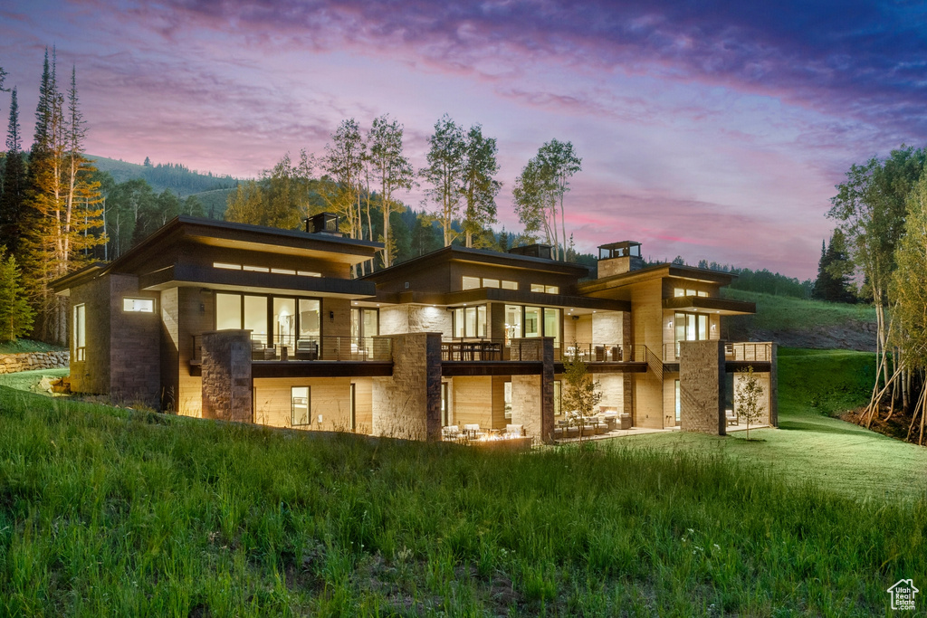 Back house at dusk with a balcony and a yard