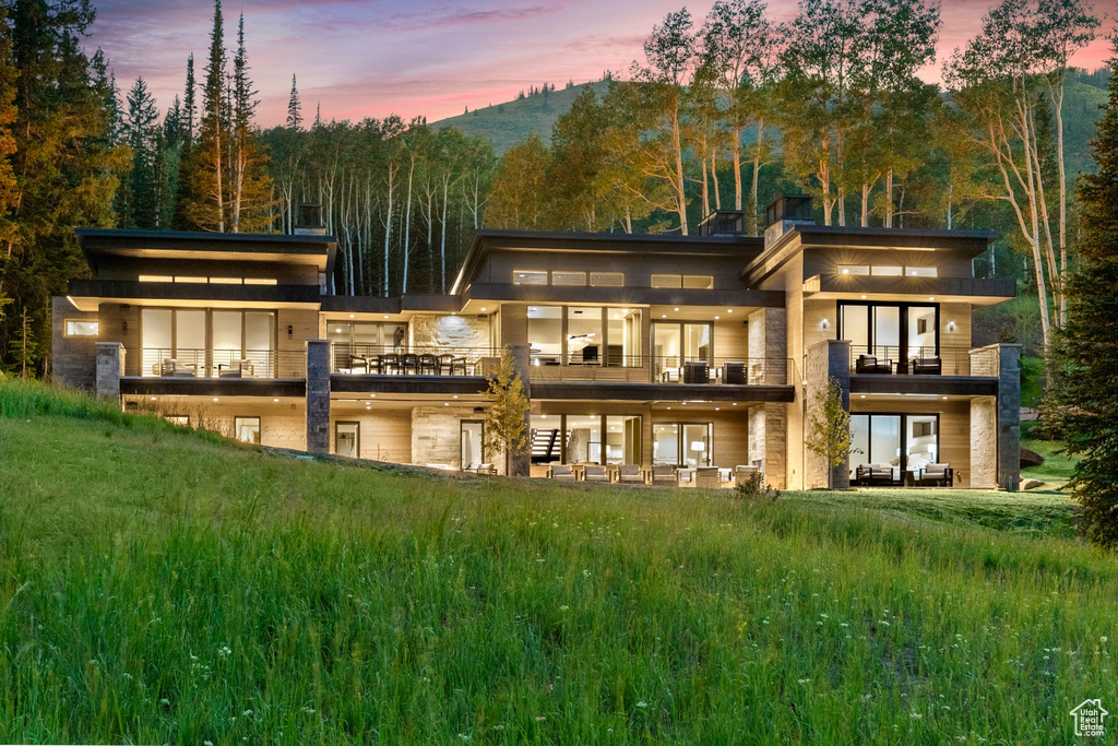 Back house at dusk with a balcony and a yard