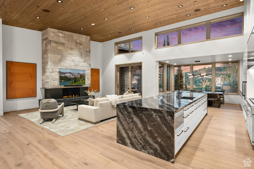 Interior space with light hardwood / wood-style floors, white cabinetry, wooden ceiling, and a stone fireplace