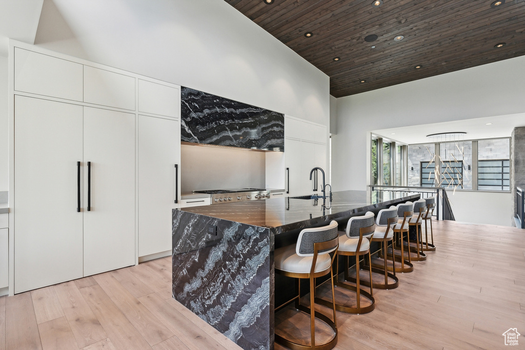 Kitchen featuring white cabinets, wood ceiling, light hardwood / wood-style floors, a large island, and a towering ceiling