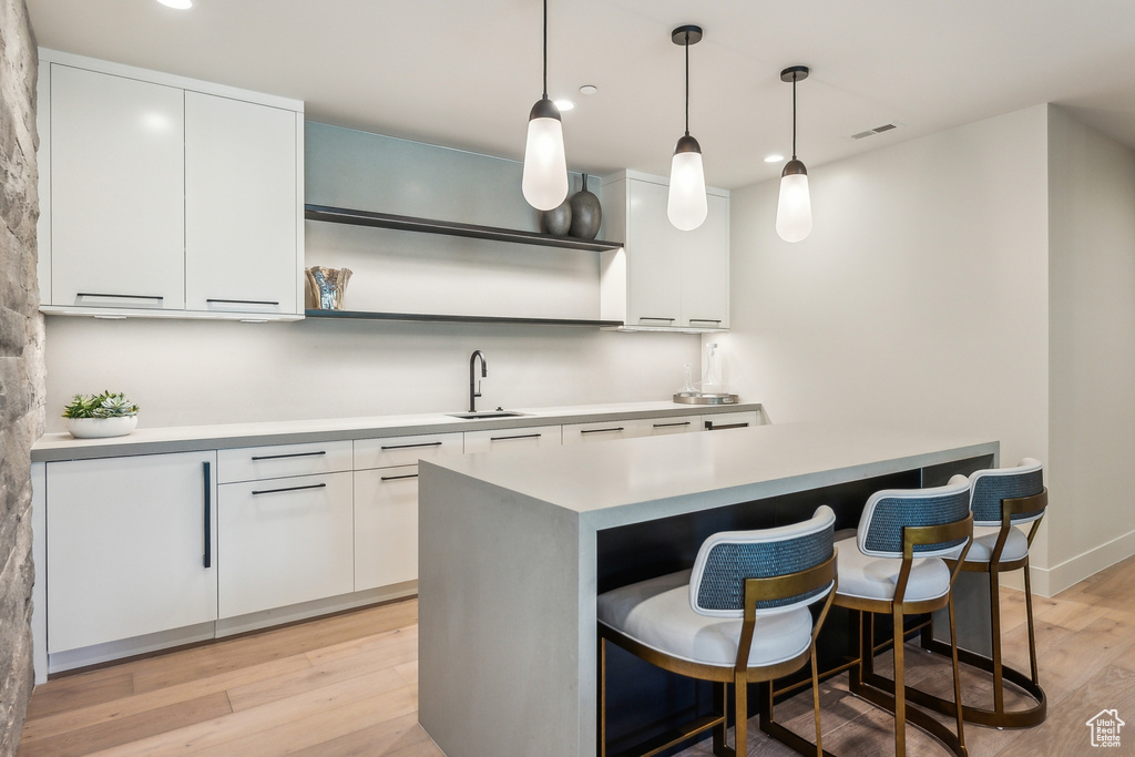 Kitchen featuring sink, white cabinetry, hanging light fixtures, and light hardwood / wood-style floors