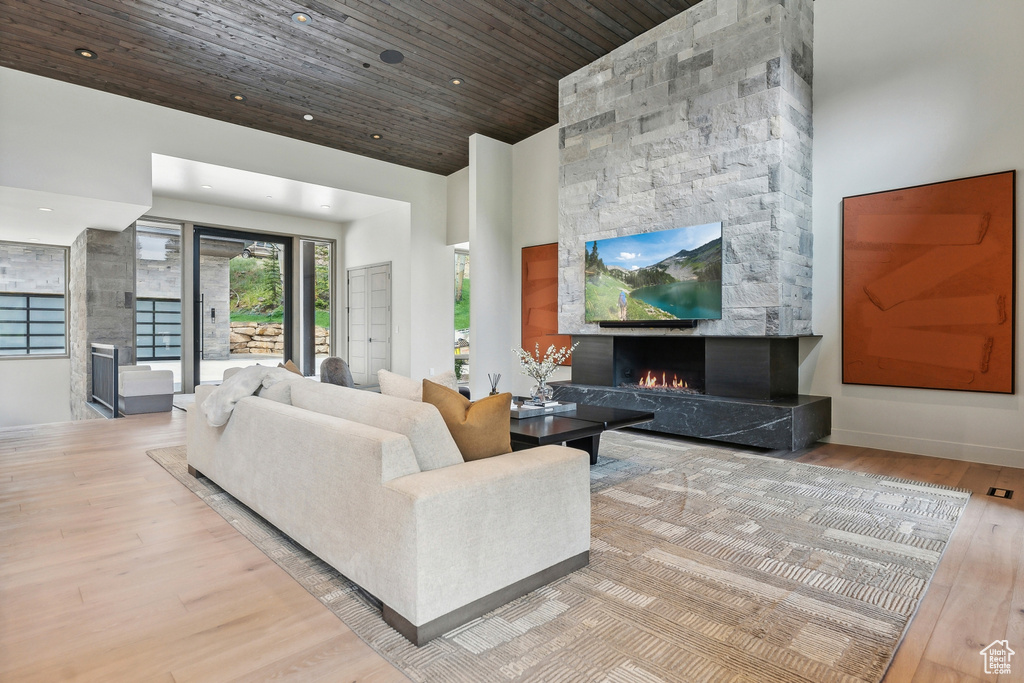 Living room with a stone fireplace, wooden ceiling, light hardwood / wood-style flooring, and a towering ceiling