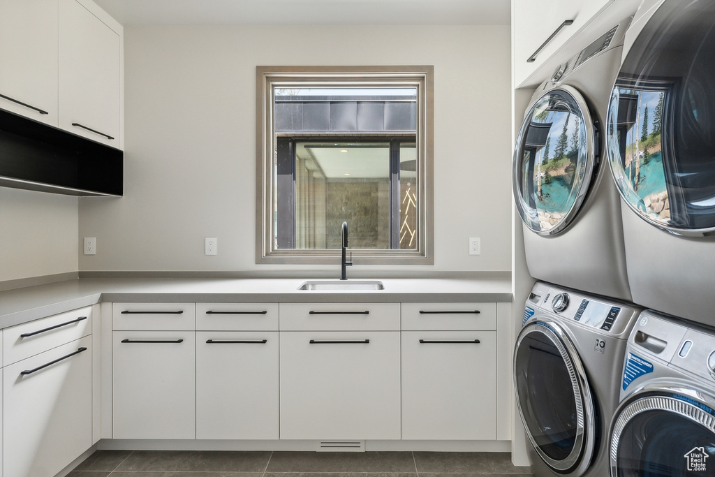 Laundry area featuring stacked washer / dryer, sink, tile patterned flooring, and cabinets