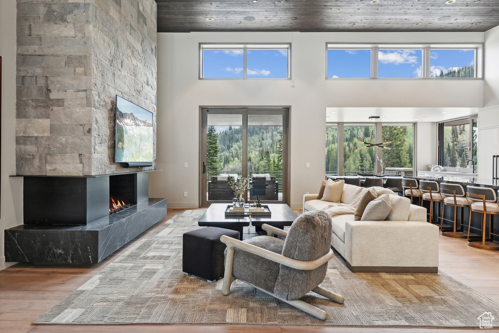 Living room featuring wooden ceiling, a stone fireplace, light wood-type flooring, and a towering ceiling