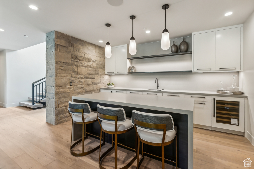 Kitchen featuring light hardwood / wood-style flooring, wine cooler, white cabinets, decorative light fixtures, and sink