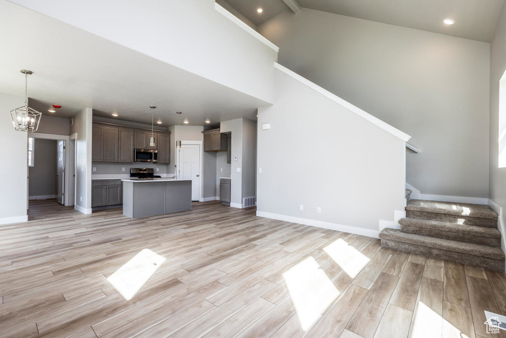 Unfurnished living room featuring beamed ceiling, light hardwood / wood-style flooring, a notable chandelier, and a towering ceiling