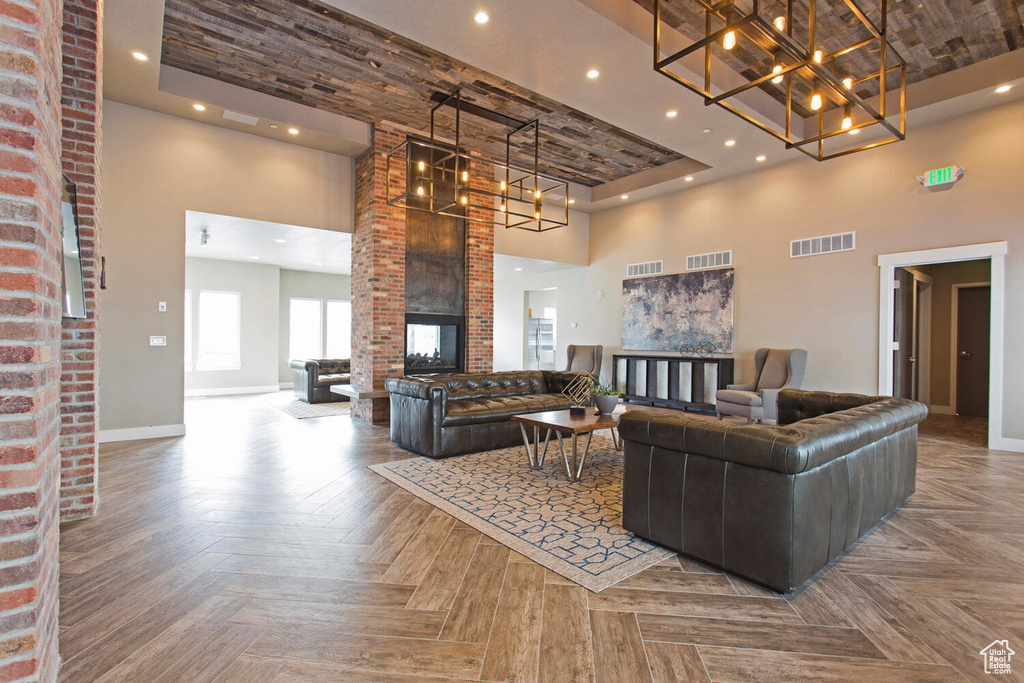 Living room with parquet floors, a fireplace, brick wall, a raised ceiling, and a towering ceiling