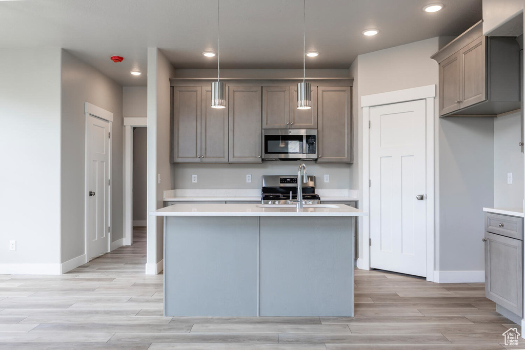 Kitchen with sink, a kitchen island with sink, stainless steel appliances, and light hardwood / wood-style floors