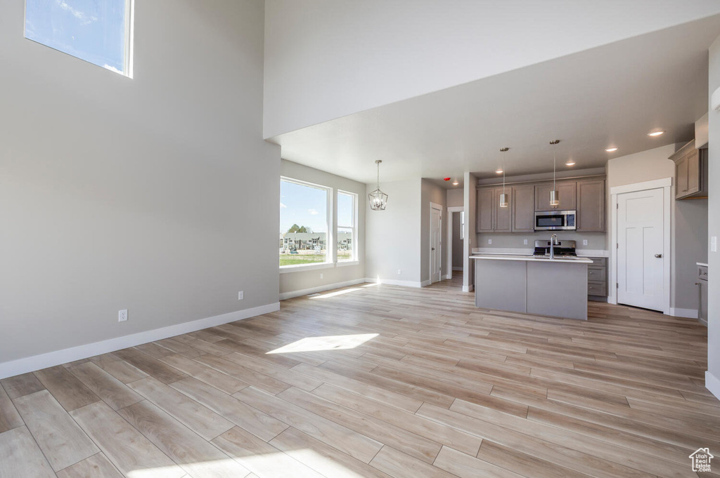 Kitchen featuring a kitchen island with sink, pendant lighting, light hardwood / wood-style floors, and a towering ceiling