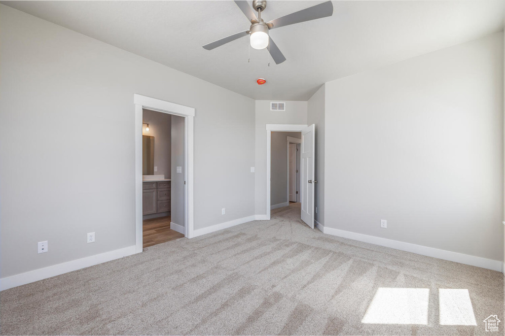 Unfurnished bedroom featuring light carpet, connected bathroom, and ceiling fan