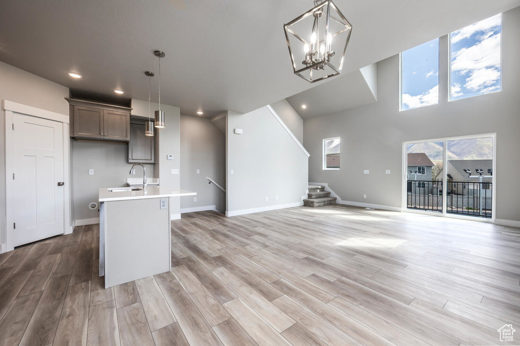 Kitchen with a notable chandelier, light wood-type flooring, an island with sink, hanging light fixtures, and sink