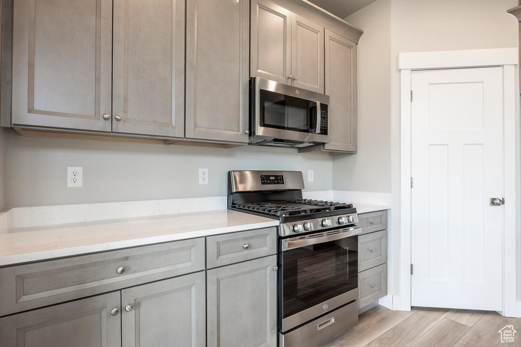 Kitchen featuring stainless steel appliances, light stone counters, and light wood-type flooring