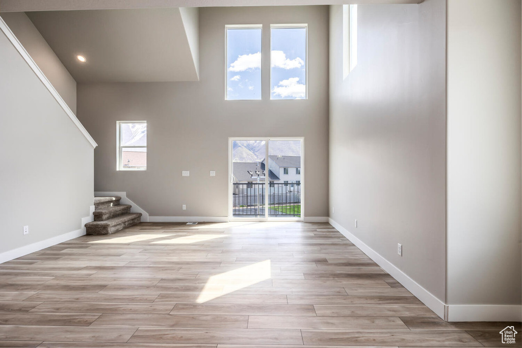 Unfurnished living room featuring a high ceiling, light wood-type flooring, and a wealth of natural light