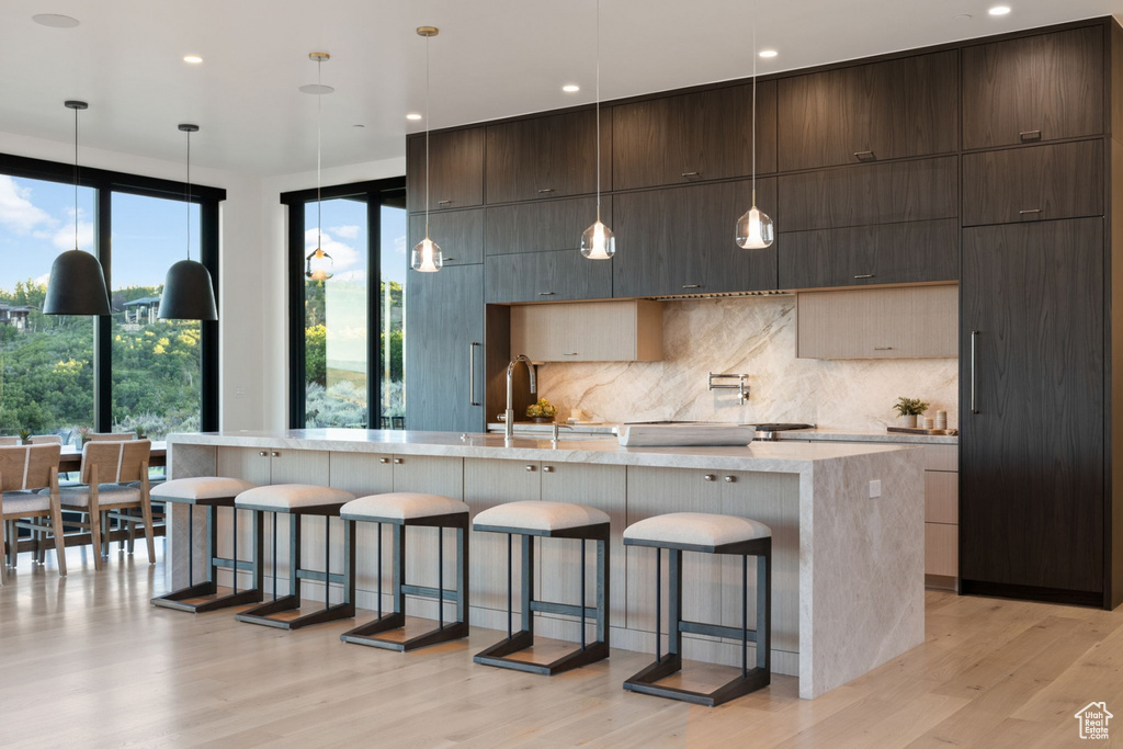 Kitchen with a breakfast bar, hanging light fixtures, light hardwood / wood-style flooring, and a large island with sink