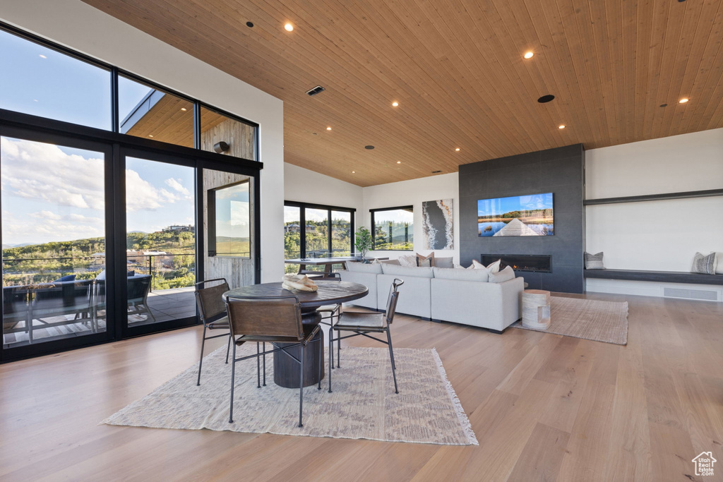 Dining area featuring a fireplace, light wood-type flooring, a towering ceiling, and wood ceiling