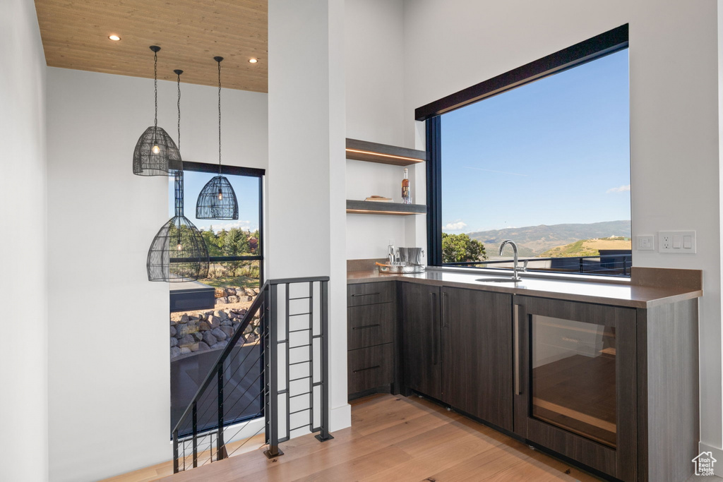 Kitchen with light wood-type flooring, pendant lighting, wood ceiling, sink, and dark brown cabinets