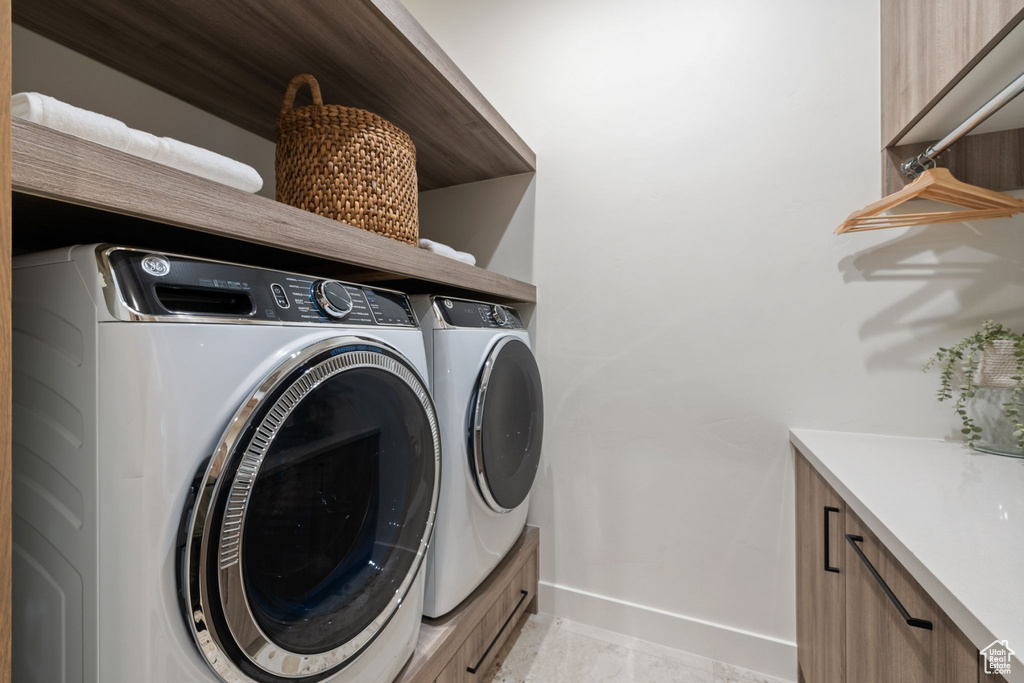 Clothes washing area featuring light tile patterned floors, washer and clothes dryer, and cabinets