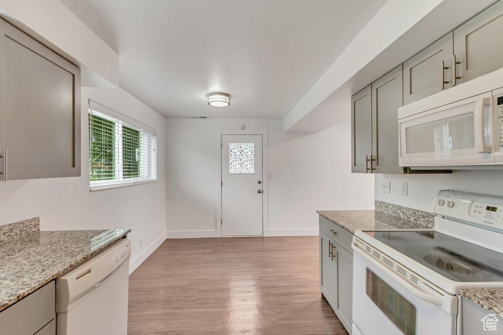 Kitchen featuring gray cabinets, light hardwood / wood-style floors, light stone counters, and white appliances