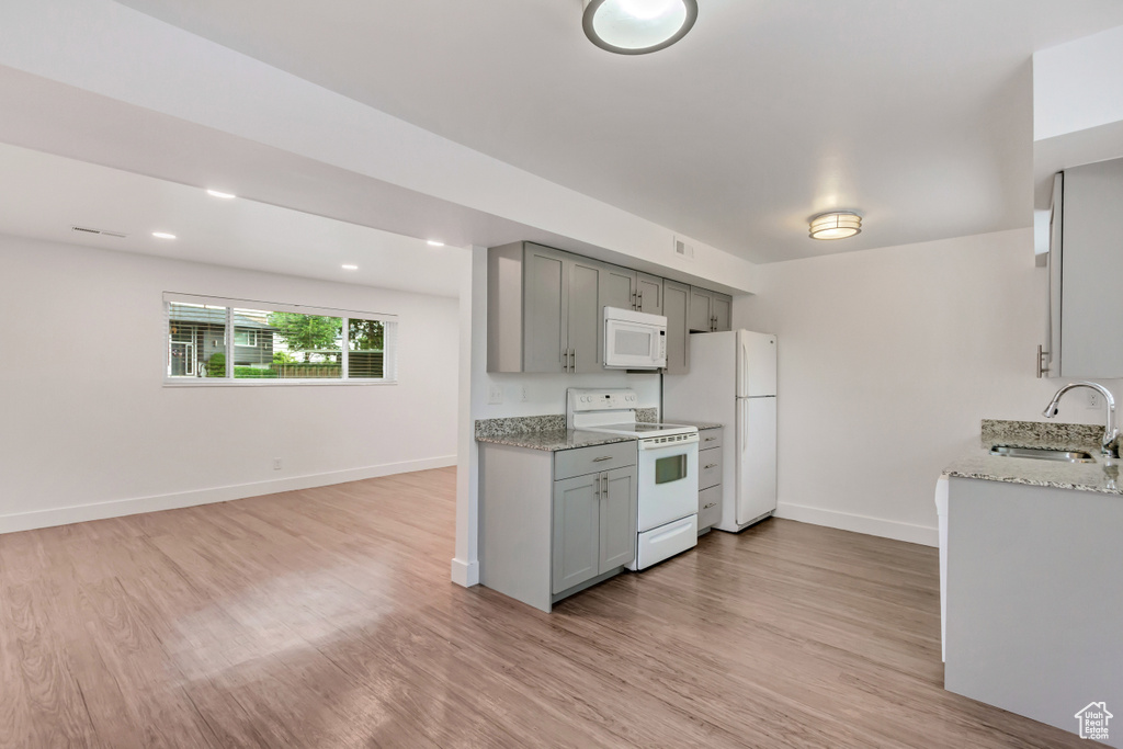 Kitchen with white appliances, light wood-type flooring, gray cabinets, light stone countertops, and sink