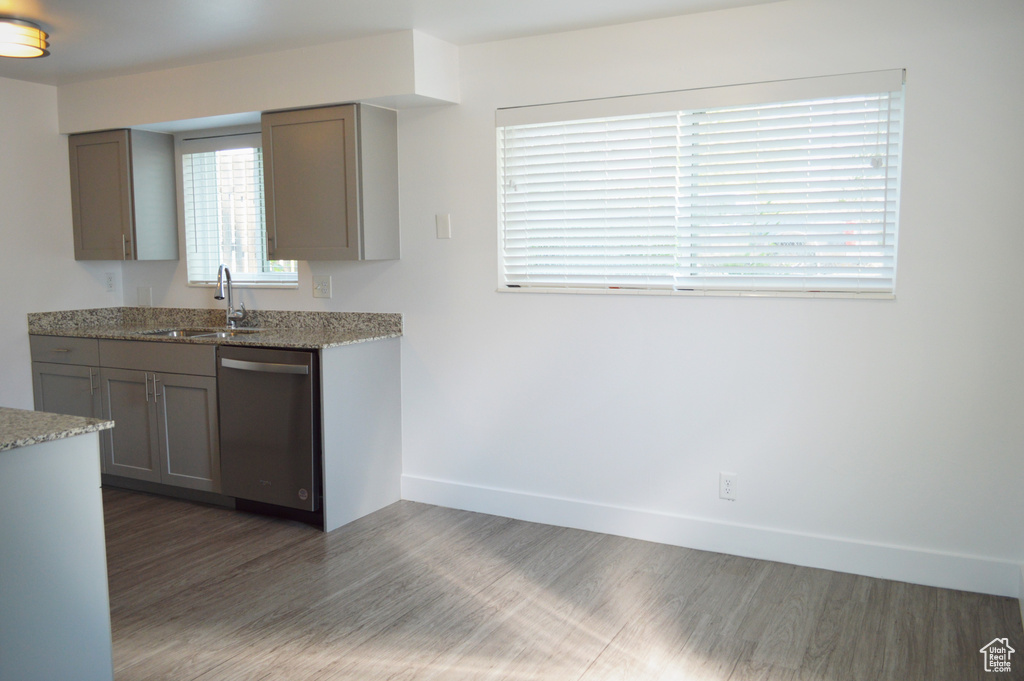 Kitchen with stainless steel dishwasher, light stone counters, sink, and dark hardwood / wood-style flooring