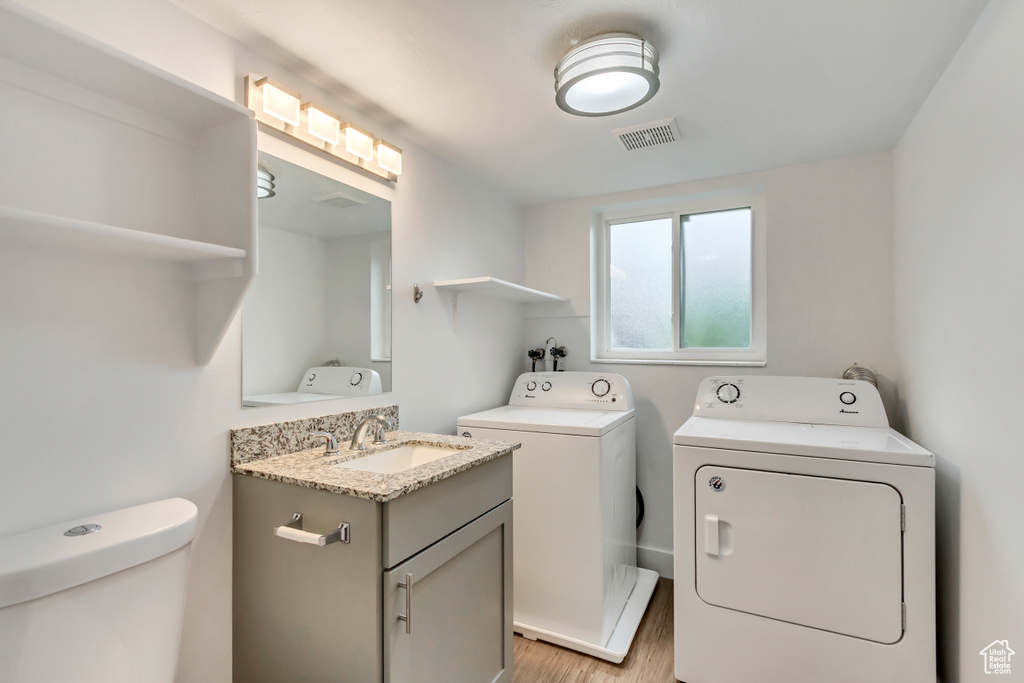 Washroom featuring washing machine and clothes dryer, light hardwood / wood-style floors, and sink