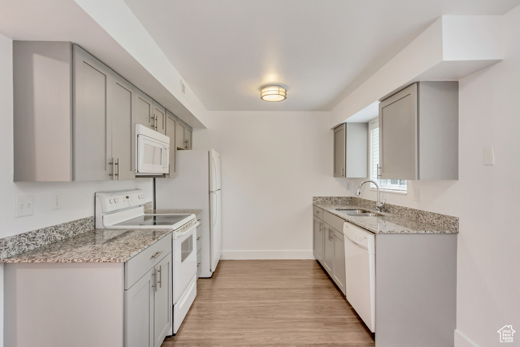 Kitchen with white appliances, sink, light stone countertops, light hardwood / wood-style floors, and gray cabinetry