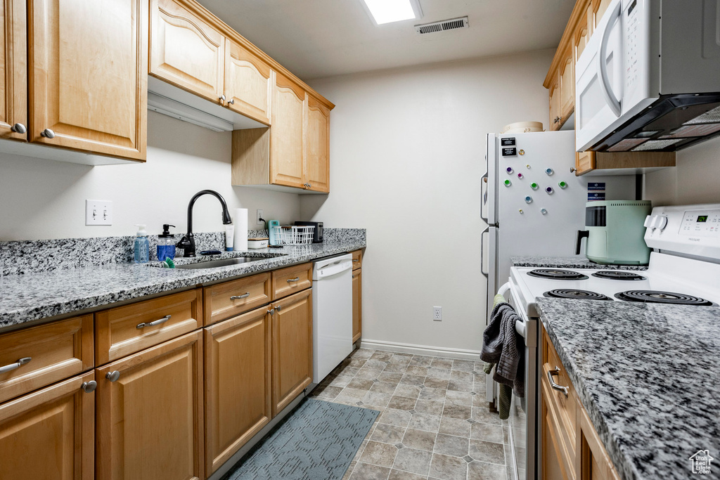 Kitchen featuring light brown cabinets, white appliances, light tile patterned floors, light stone counters, and sink