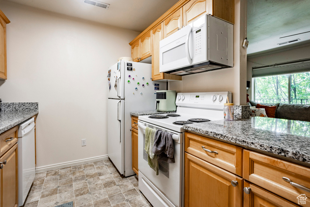 Kitchen with light brown cabinets, light stone counters, white appliances, and light tile patterned floors