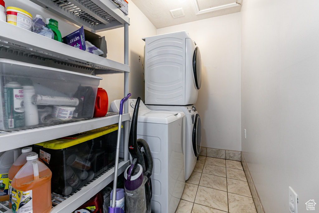 Laundry area with stacked washer and clothes dryer and light tile patterned flooring