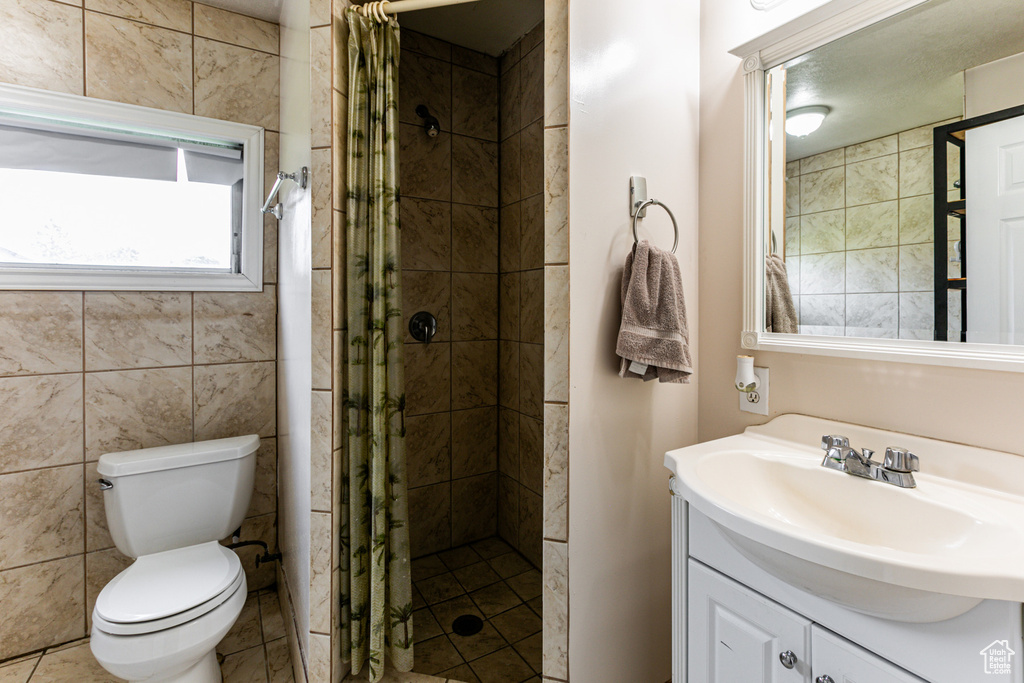 Bathroom with walk in shower, tile patterned flooring, toilet, vanity, and tile walls