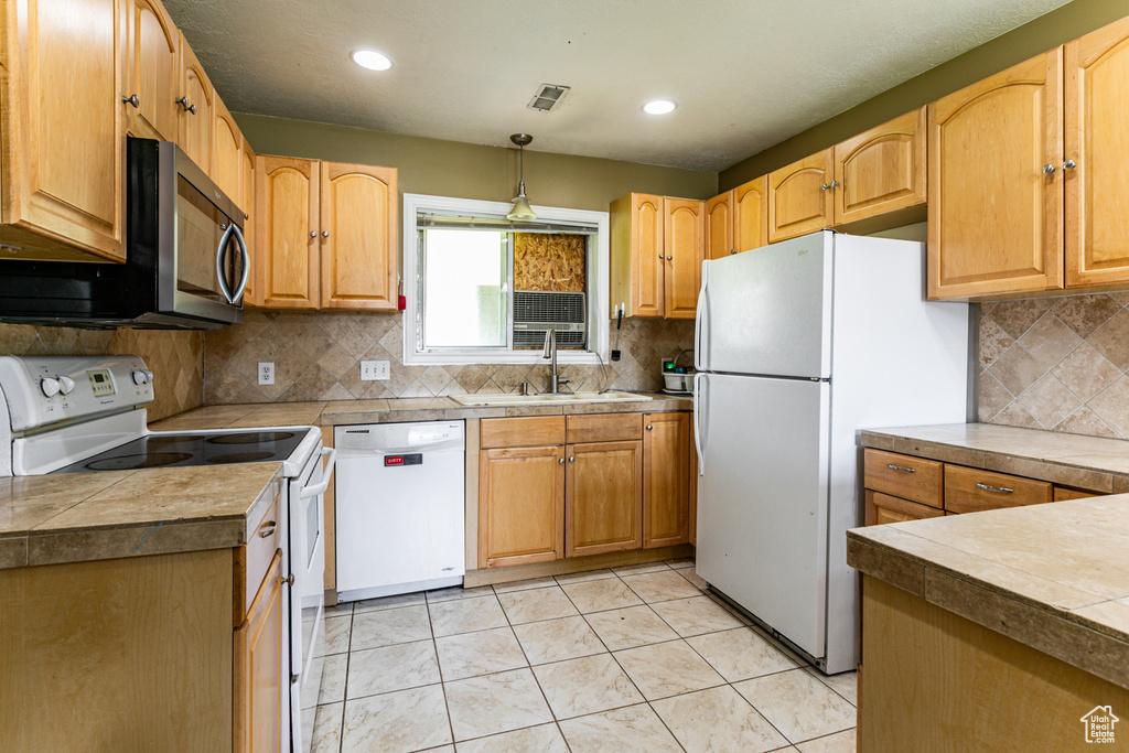 Kitchen with tasteful backsplash, white appliances, sink, decorative light fixtures, and light tile patterned floors