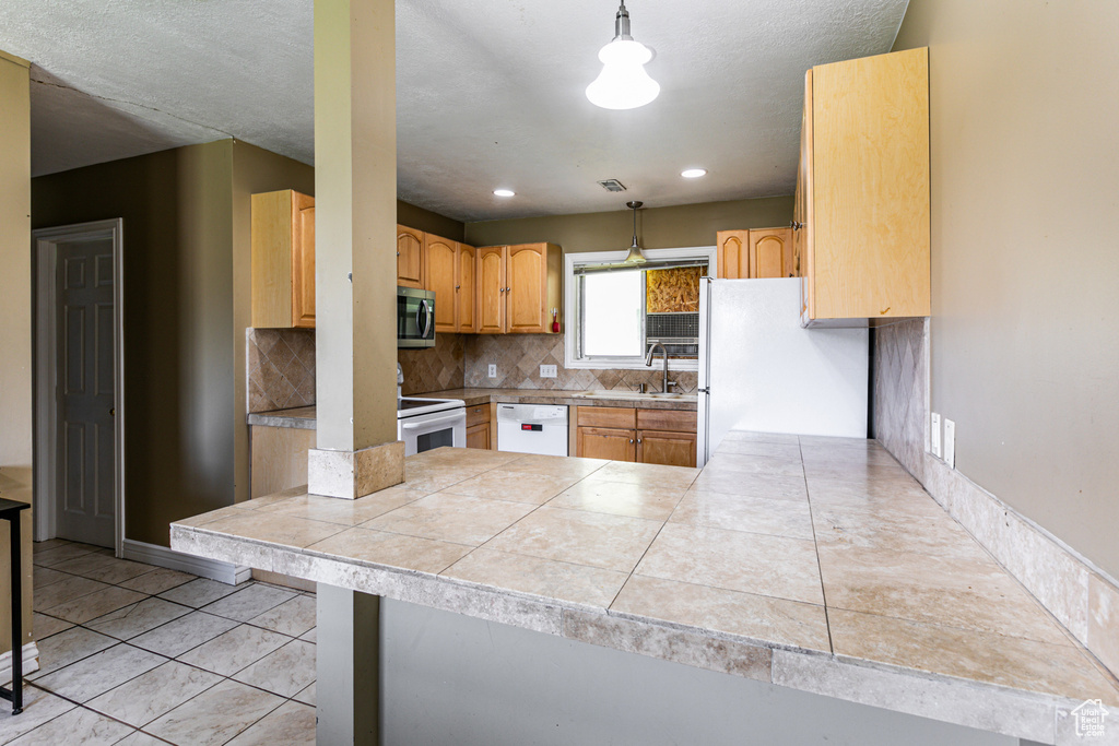 Kitchen featuring hanging light fixtures, sink, backsplash, and white appliances