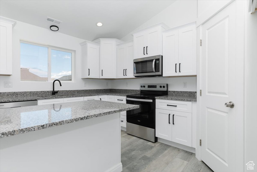 Kitchen featuring appliances with stainless steel finishes, sink, light wood-type flooring, light stone countertops, and white cabinets