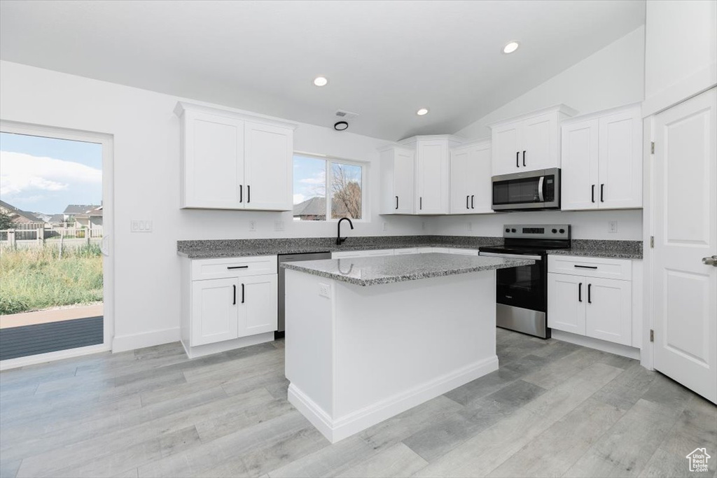 Kitchen featuring white cabinetry, a center island, stainless steel appliances, and lofted ceiling