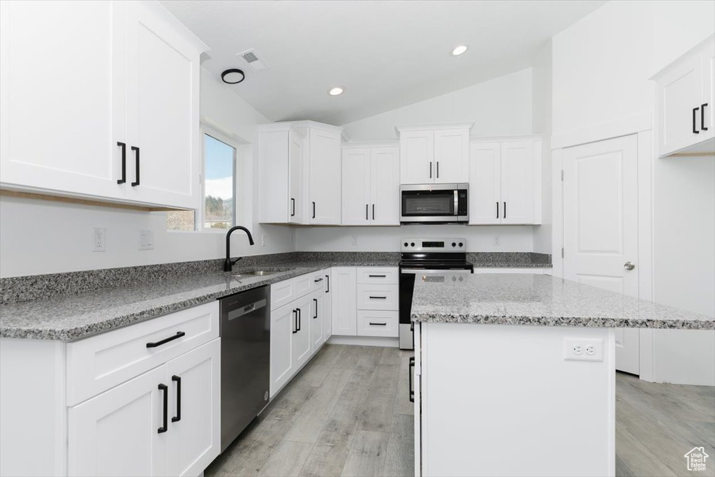 Kitchen featuring light wood-type flooring, vaulted ceiling, dishwasher, range with electric cooktop, and white cabinets