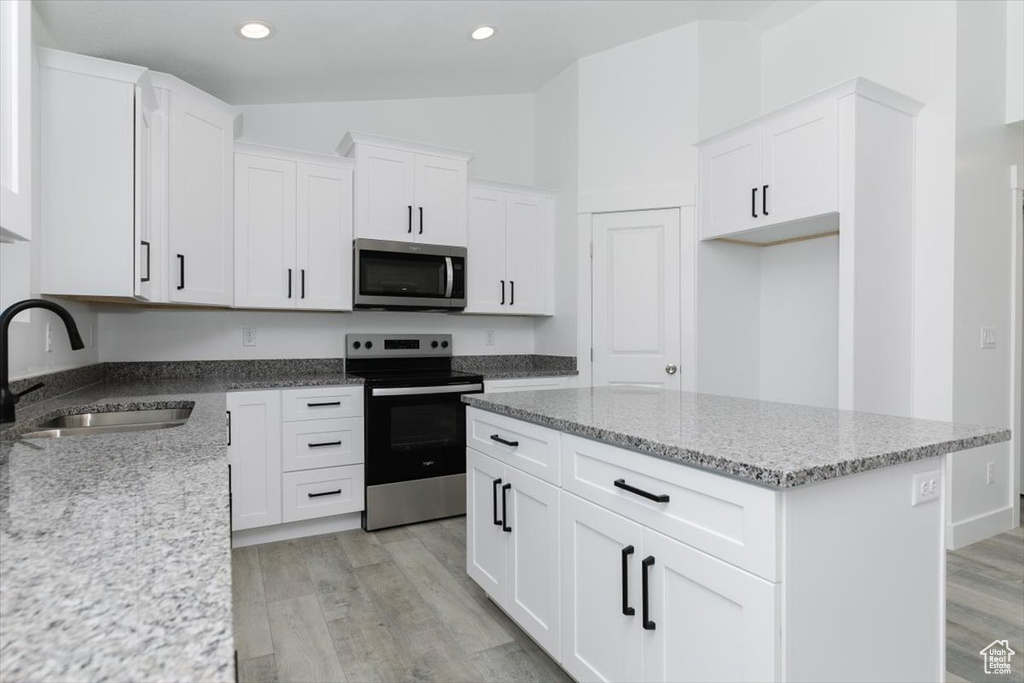 Kitchen with sink, light wood-type flooring, vaulted ceiling, and stainless steel appliances