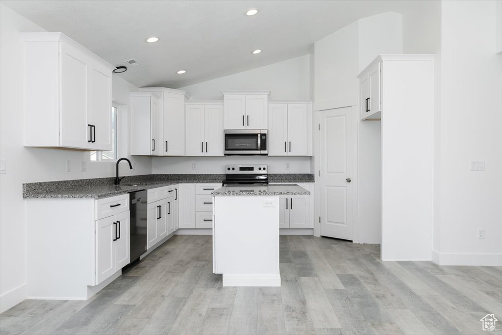 Kitchen featuring white cabinets, a center island, range, black dishwasher, and lofted ceiling