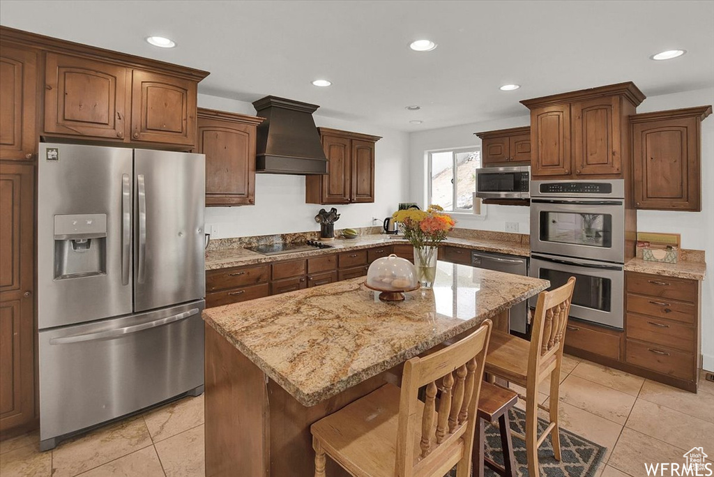 Kitchen featuring appliances with stainless steel finishes, light tile patterned flooring, custom exhaust hood, and a kitchen island