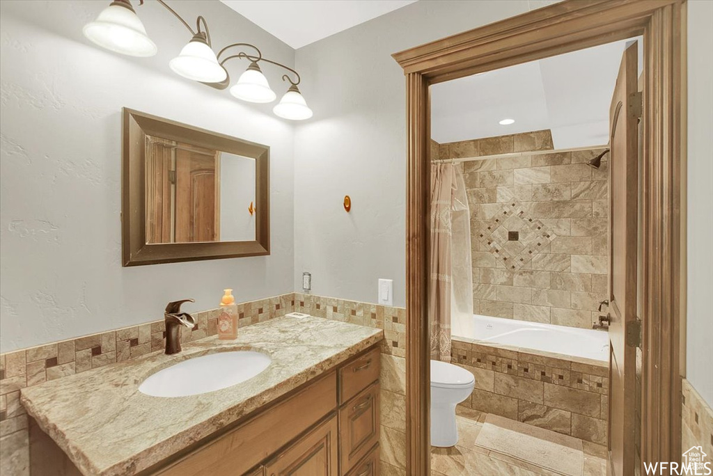 Full bathroom featuring toilet, vanity, tile walls, shower / bath combo with shower curtain, and tile patterned floors