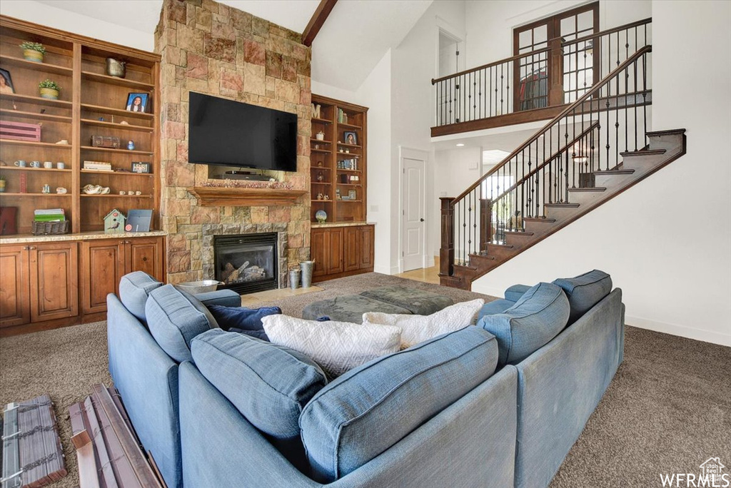 Carpeted living room featuring a fireplace, beamed ceiling, built in shelves, and a towering ceiling