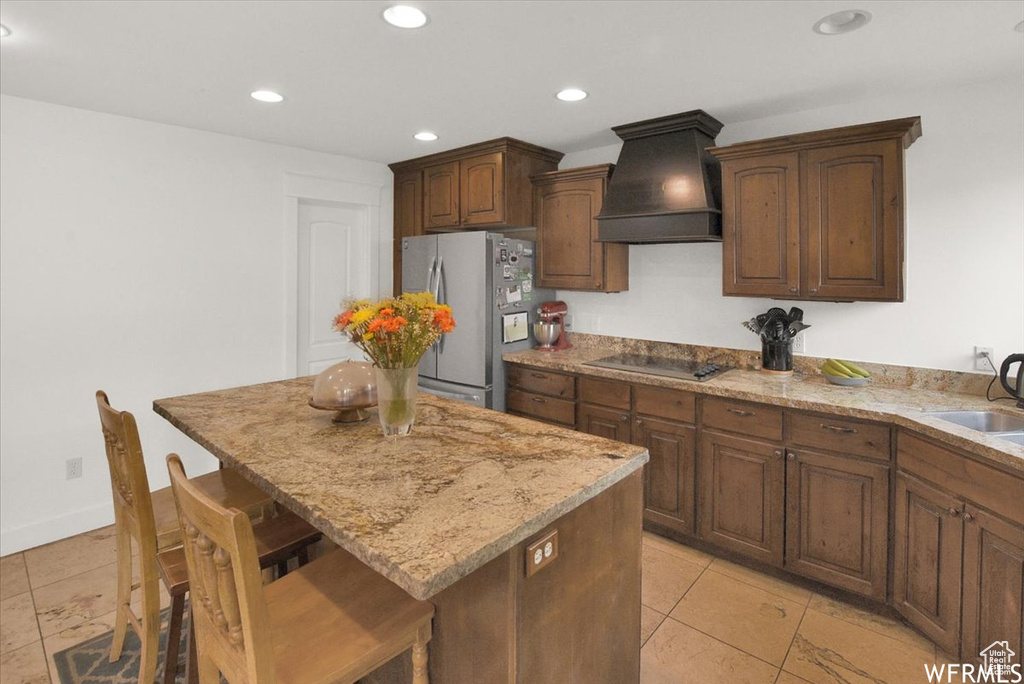 Kitchen with a center island, stainless steel fridge, light tile patterned floors, and premium range hood