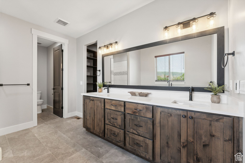 Bathroom featuring toilet, tile patterned floors, and dual bowl vanity