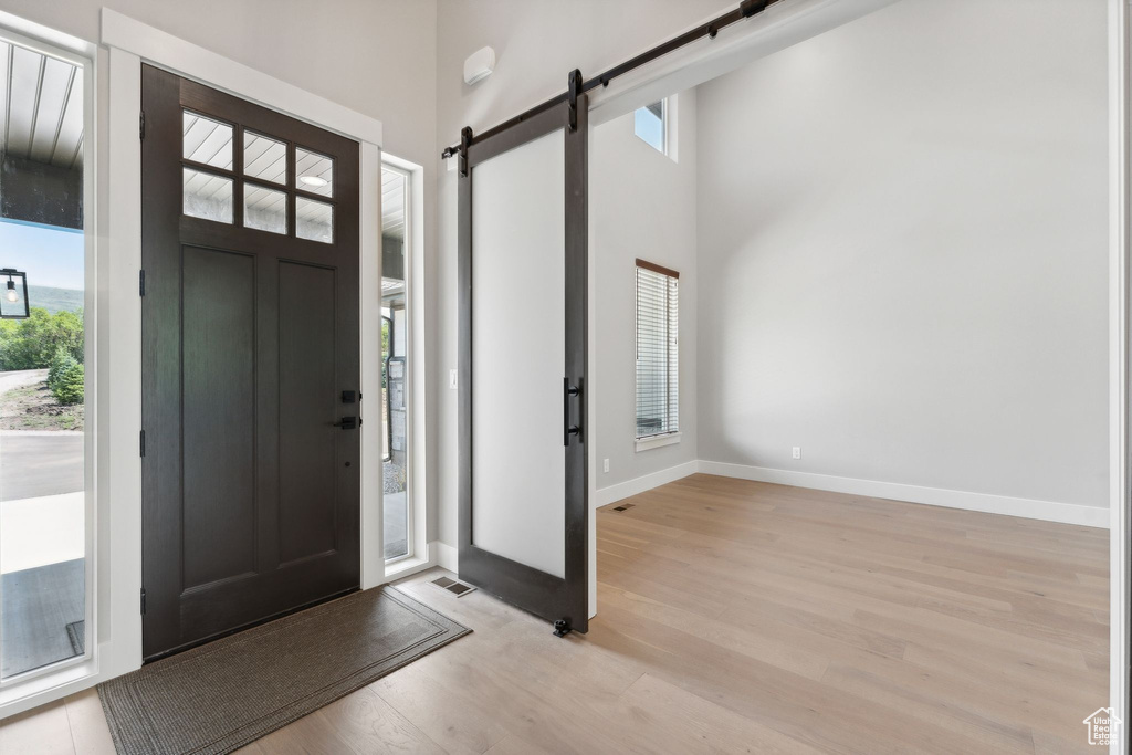 Foyer entrance featuring light hardwood / wood-style flooring, a barn door, a wealth of natural light, and a high ceiling