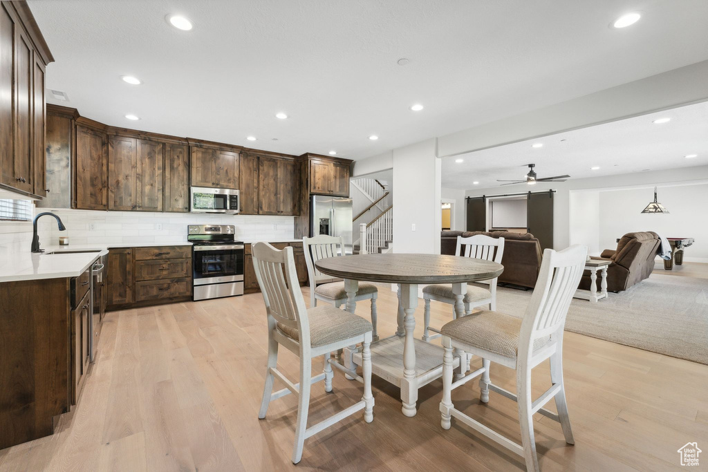 Kitchen with light wood-type flooring, backsplash, ceiling fan, appliances with stainless steel finishes, and sink