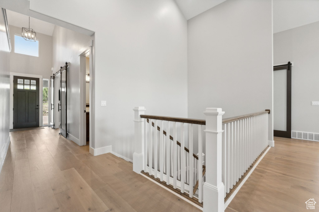 Hallway with light hardwood / wood-style floors, a notable chandelier, a towering ceiling, and a barn door