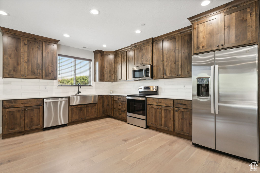 Kitchen with appliances with stainless steel finishes, light hardwood / wood-style flooring, sink, dark brown cabinets, and decorative backsplash