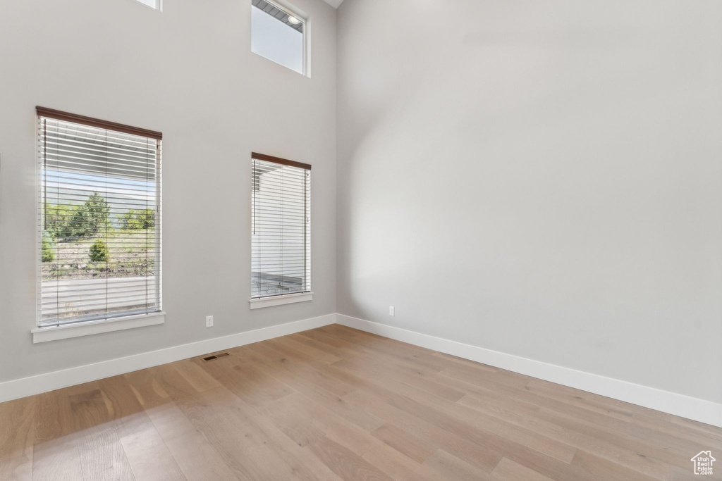 Unfurnished room with plenty of natural light, light hardwood / wood-style floors, and a towering ceiling