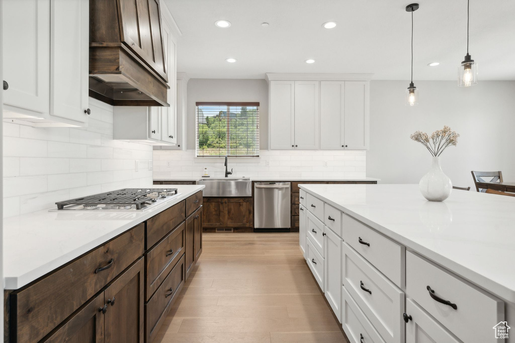 Kitchen with dark brown cabinets, custom exhaust hood, appliances with stainless steel finishes, decorative backsplash, and sink